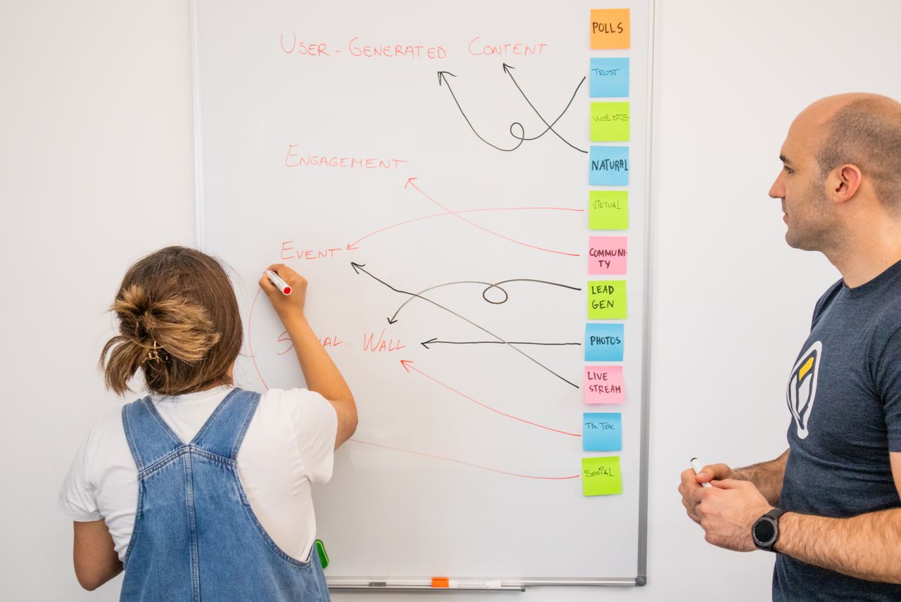 Deux collègues élaborent ensemble une stratégie marketing devant un tableau blanc, en se concentrant sur le contenu généré par les utilisateurs.